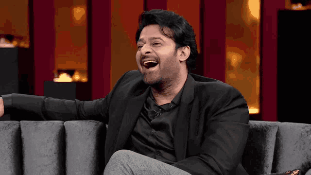 a man in a suit is sitting on a couch laughing