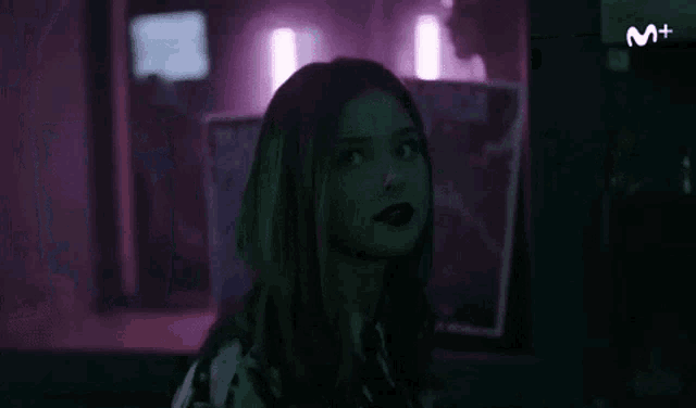 a young woman is standing in a dark room with purple lights .