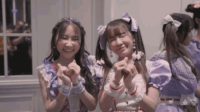 two girls in purple dresses are making hearts with their fingers