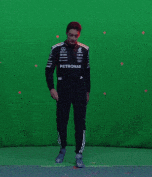 a man in a petronas racing suit is standing in front of a green screen