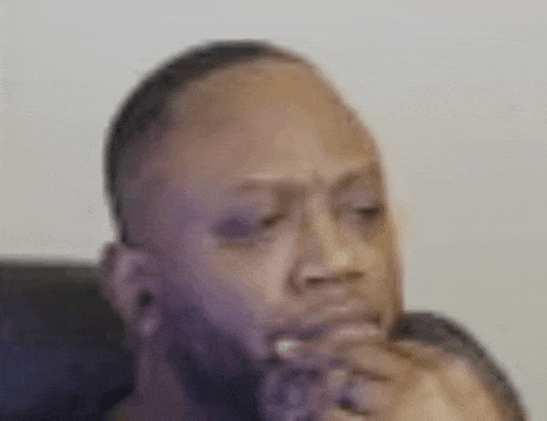 a man with a beard is sitting in a chair with his hand on his chin and looking at the camera .