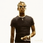 a man wearing sunglasses and a black shirt is standing in front of a white wall .