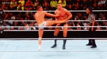 two men are wrestling in a wrestling ring with a referee in the background .