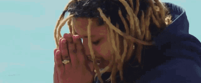 a man with dreadlocks is praying with his hands folded in front of his face .