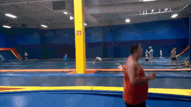 a man in a red tank top stands on a trampoline in front of a sign that says ' no diving '