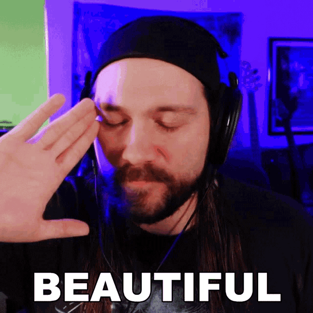 a man wearing headphones and a beanie is making a gesture with his hand in front of a sign that says beautiful