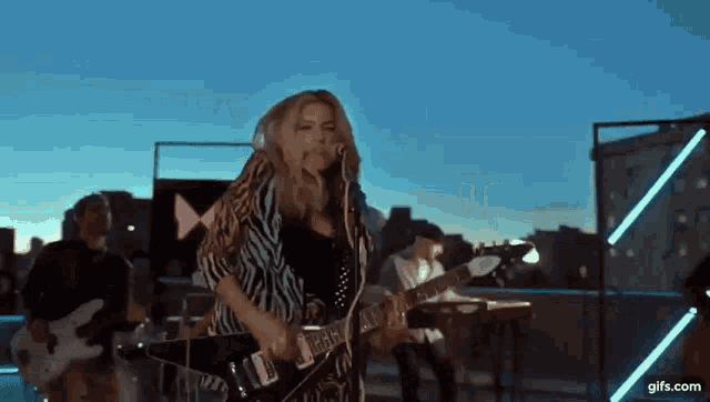 a woman is playing a guitar and singing into a microphone while a band plays behind her .