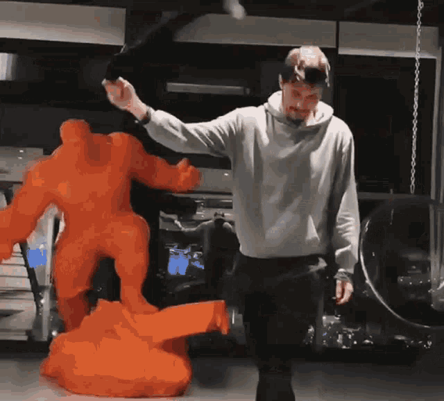 a man in a grey sweatshirt stands in front of a statue of a man