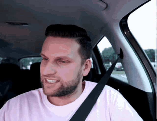 a man wearing a pink shirt and a black seat belt smiles