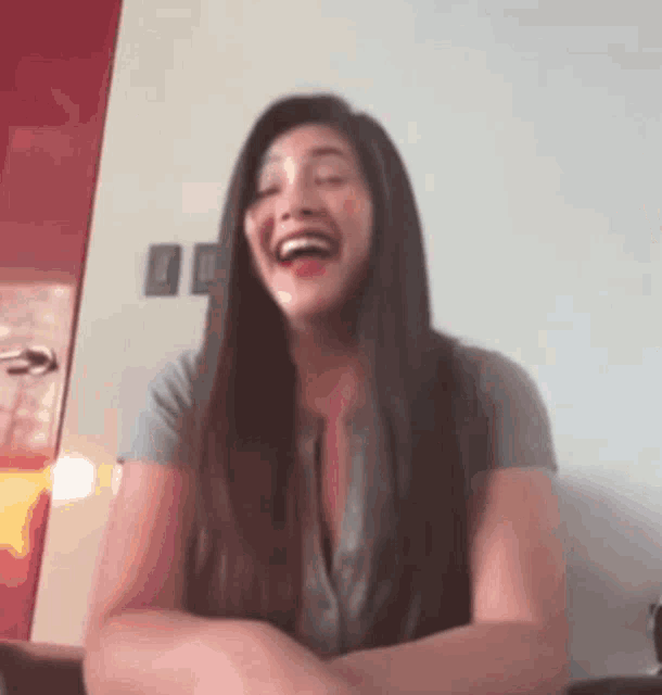 a woman with long hair is laughing while wearing a gray shirt