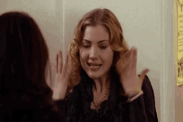 a woman is standing next to another woman in front of a wall and holding her hair .