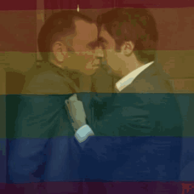 two men are kissing each other in front of a rainbow flag .