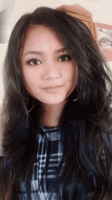 a woman with long dark hair is wearing a plaid top