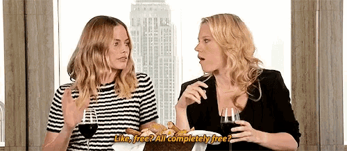 two women are sitting at a table talking to each other while drinking wine .