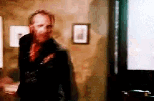 a man in a black jacket and red tie is standing in a dark room