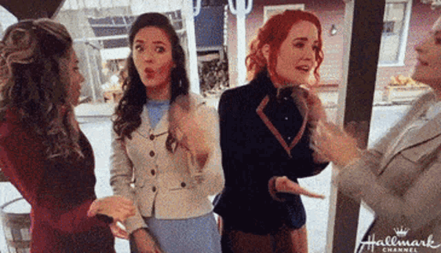 three women are standing next to each other in front of a building and talking to each other .