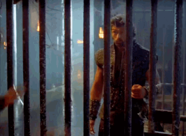 a man is standing in a cage behind bars .