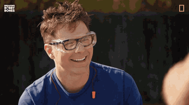 a man wearing glasses is smiling in front of a breaking bobby bones poster