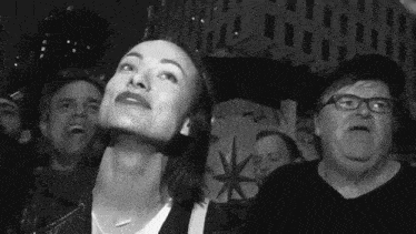 a woman is looking up at the sky while standing in a crowd of people at a protest .