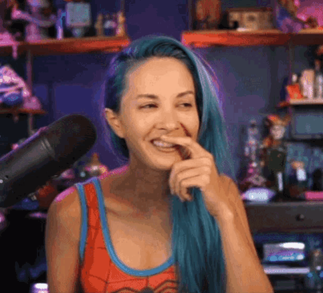 a woman with blue hair is smiling in front of a microphone while wearing a spiderman tank top .
