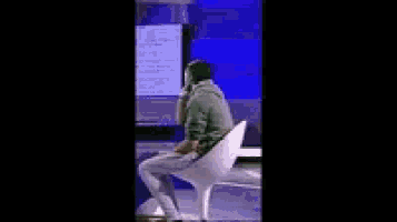 a man is sitting in a white chair in front of a computer monitor .