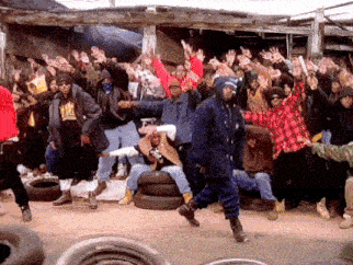 a group of people are dancing in front of a building with tires