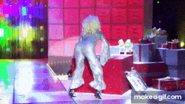 a woman in a silver jumpsuit is dancing on a stage surrounded by gifts