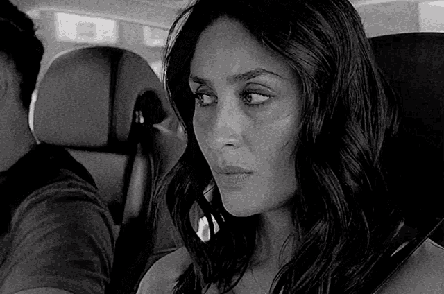 a black and white photo of a woman sitting in a car with a man behind her