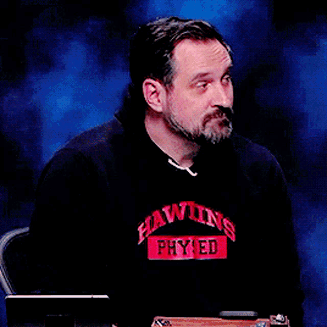 a man wearing a black shirt that says hawkins phy ed on it
