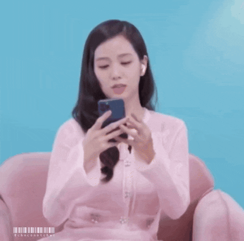 a woman in a pink dress is sitting on a pink chair looking at her phone .