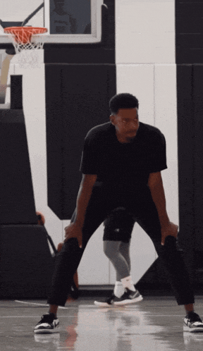 a man in a black shirt is standing on a basketball court with his hands on his knees