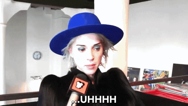 a woman wearing a blue hat is talking into a microphone and says " uhhhh "