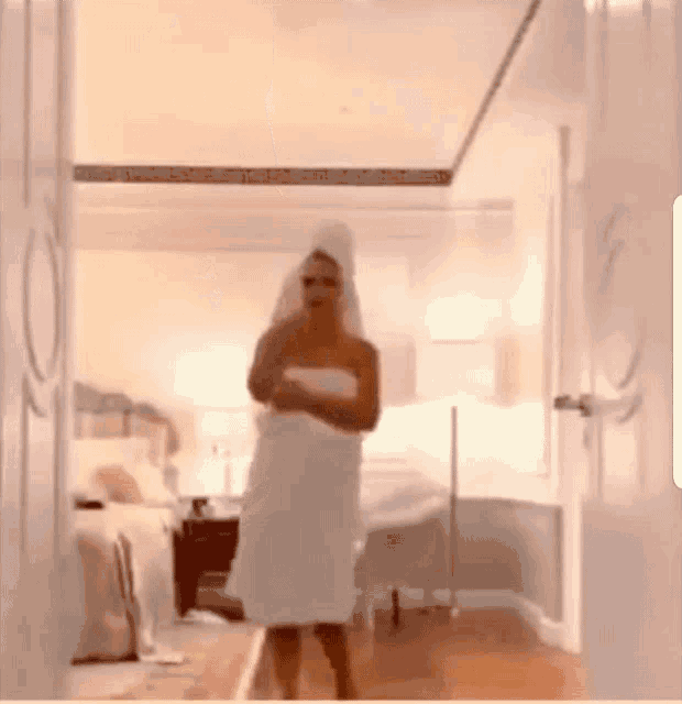 a woman wrapped in a towel is standing in a bathroom .
