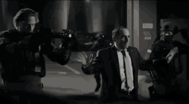 a man in a suit and tie is being escorted by a group of men with guns