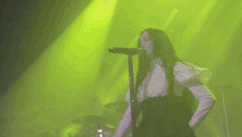 a woman singing into a microphone with a green background