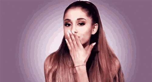 ariana grande is covering her mouth with her hand in front of a purple background .