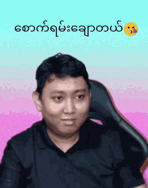 a man in a black shirt is sitting in a chair with a pink background and a smiley face in the corner
