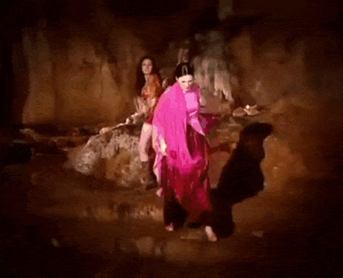 a woman in a pink cape is surrounded by flames while another woman stands behind her .