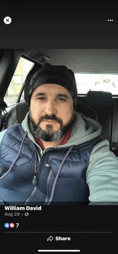 a man with a beard is sitting in a car wearing a hat