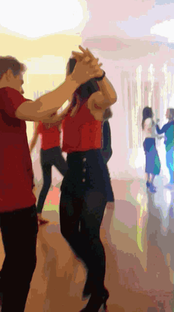 a man in a red shirt is dancing with a woman in black pants