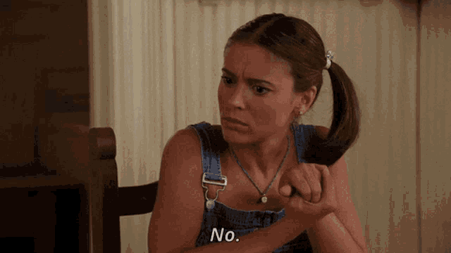 a woman in overalls holds her hair in a pigtail and says no