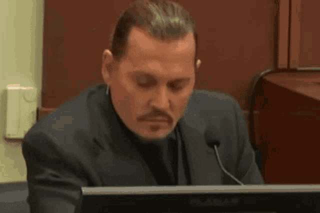 a man in a suit is sitting at a desk in front of a microphone .