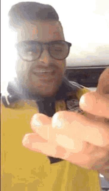a man wearing glasses and a yellow shirt is smiling and making a funny face .