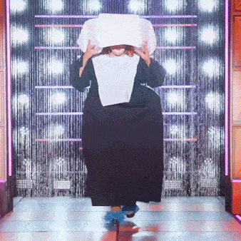a woman in a nun costume is walking down a runway with a pillow on her head .