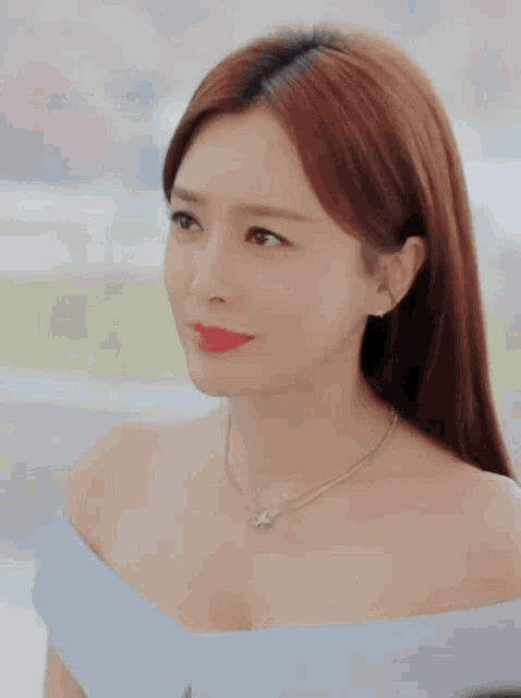 a woman wearing a blue off the shoulder top and a star necklace smiles