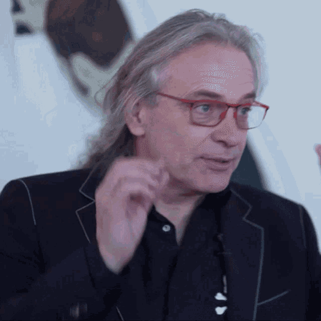 a man with long hair and glasses is wearing a black suit