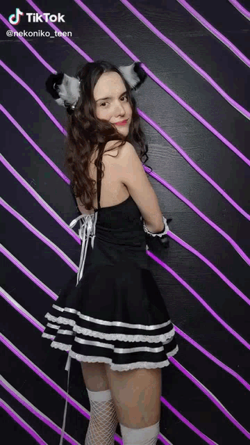 a girl in a black and white dress with cat ears is standing in front of a striped wall .