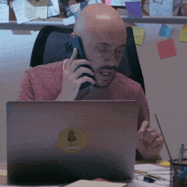 a man talking on a cell phone in front of a laptop with a sticker on it