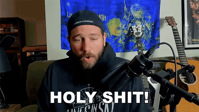 a man sitting in front of a microphone with the words holy shit written on his shirt