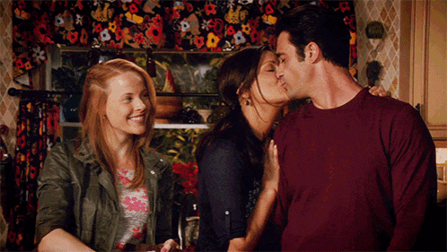 a man kisses a woman on the cheek while two women look on